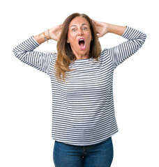 Poster - Beautiful middle age woman wearing stripes sweater over isolated background Crazy and scared with hands on head, afraid and surprised of shock with open mouth