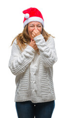 Poster - Middle age senior hispanic woman wearing christmas hat over isolated background smelling something stinky and disgusting, intolerable smell, holding breath with fingers on nose. Bad smells concept.