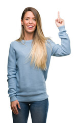 Wall Mural - Beautiful young woman wearing sweater and jeans surprised with an idea or question pointing finger with happy face, number one