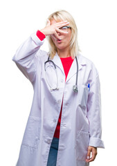 Poster - Young beautiful blonde doctor woman wearing medical uniform over isolated background peeking in shock covering face and eyes with hand, looking through fingers with embarrassed expression.