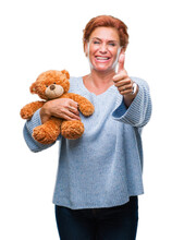 Senior caucasian woman holding teddy bear over isolated background happy with big smile doing ok sign, thumb up with fingers, excellent sign