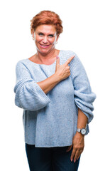 Poster - Atrractive senior caucasian redhead woman wearing winter sweater over isolated background cheerful with a smile of face pointing with hand and finger up to the side with happy and natural expression