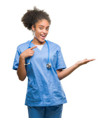 Canvas Print - Young afro american doctor woman over isolated background amazed and smiling to the camera while presenting with hand and pointing with finger.