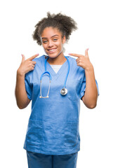 Sticker - Young afro american doctor woman over isolated background smiling confident showing and pointing with fingers teeth and mouth. Health concept.