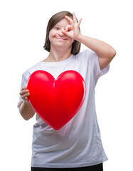 Sticker - Young adult woman with down syndrome holding red heart over isolated background with happy face smiling doing ok sign with hand on eye looking through fingers