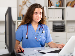 Wall Mural - Young positive brunette female doctor with stethoscope working in medical office