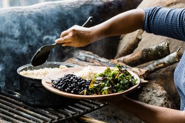 Hands of an unrecognizable woman serving a plate of rice with beans and salad in a traditional kitchen.