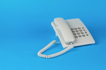 A white telephone with gray buttons on a blue background.