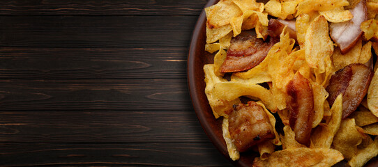 Potato chips with bacon on a plate on a wooden background