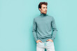 © halayalex - Portrait of handsome confident  model. Sexy stylish man dressed in  sweater and jeans. Fashion hipster male with curly hairstyle posing near blue wall in studio. Isolated