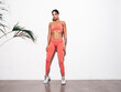 © halayalex - Tanned fitness woman in pink sports clothing. Sexy young smiling beautiful model with perfect body.Female isolated on white background in studio. Stretching out before training. Near wall. Full length