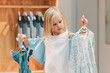Child, fashion and shopping while choosing kids clothing in a shop, store or boutique with a cute girl holding dresses thinking or picking color choice. Little kid shopper or customer buying clothes