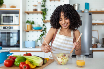 Wall Mural - Happy smiling cute woman is preparing a fresh healthy vegan salad with many vegetables in the kitchen at home and trying a new recipe