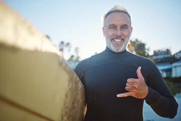 Beach, surf board and a happy elderly surfer man with hand sign and smile. Freedom, water sports and happiness, fun on retirement holiday in Australia. Health, fitness and senior ready for surfing.