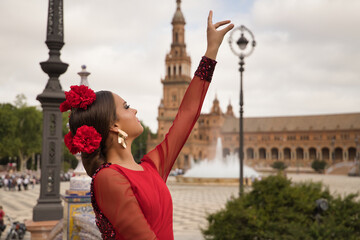 Sticker - Young teenage woman in red dance suit with red carnations in her hair doing flamenco dance poses. Flamenco concept, dance, art, typical Spanish dance.