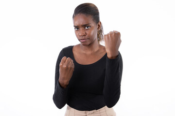 Wall Mural - Portrait of aggressive African American woman with clenched fists. Angry young model in black shirt with ponytail looking at camera, ready to fight. Anger, fight concept.