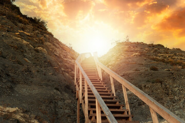 Religion and motivation. A wooden steep staircase in the mountain leading to the sky, with bright sunlight and sunset. Bottom view. The concept of paradise, victory and hope for a bright future