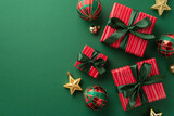 Fototapeta  - Christmas presents concept. Top view photo of gift boxes with ribbon bows red green gold baubles and star ornaments on isolated green background