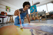 © S Fanti/peopleimages.com - Art, creative and painter painting with watercolor and brush on a canvas at a table in a work studio. Indian design artist, woman or creativity student working as a designer with paint in a workshop