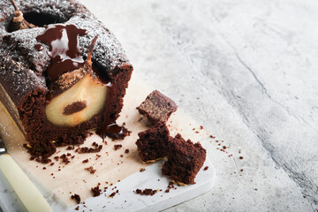 Chocolate cake with pears baked inside. Chocolate pear cake or dark chocolate bundt cake with pear on light gray table at home. Home cooking and baking recipes concept. Selective focus.