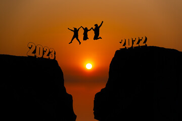 Silhouette group of business woman  jumping over a cliff, skipping 2022 into 2023 on the background of a new morning, happy New year concept.