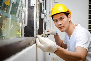 Handsome Asian builder wearing a yellow helmet Measuring window lengths for home improvements. Construction concept, renovating the house to be beautiful