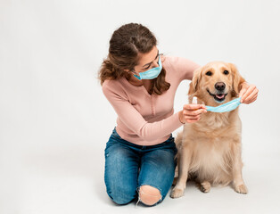 Wall Mural - Female woman in medical protected face mask disinfects dogs paws with a sanitizer. A dog smile looks at camera with mask isolated on white background. Pets hygiene concept