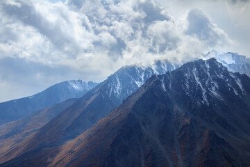 Wall Mural - Alpine rocky peaks with snow, the sky is covered with clouds, the sun shines through the clouds, illuminating the mountain slopes, autumn in the mountains