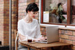 © Andriy Medvediuk - Young businesswoman working on laptop at cafe on terrace in urban city, stylish outfit with white blouse and skirt. Coffee break, business concept. Working outdoors. Remote job.