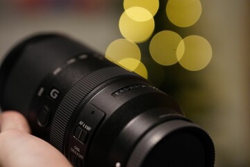 Sticker - Closeup of a hand holding a specialized professional camera lens with bright yellow bokeh behind it