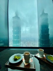 Sticker - Cup of coffee and dessert with a foggy view of skyscrapers from the window