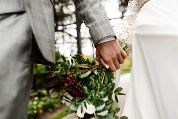 Wall Mural - Wedding. The groom in a suit and the bride in a white dress standing side by side and are holding bouquets of white flowers and greenery