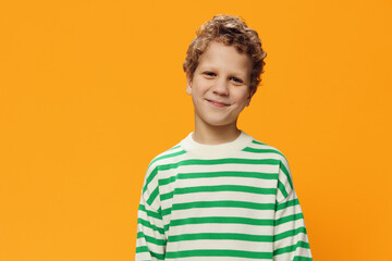 horizontal portrait of a cute curly boy of school age in a striped long-sleeved t-shirt on an orange background