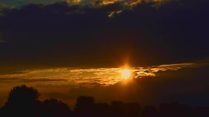 Wall Mural - Timelapse of an Orange Sunset With Many Low Clouds Hiding and Peeking the Sun