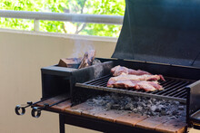 Making A Barbecue With A Portbale Grill In The Balcony Of Apartment. Traditional Roast Beef Of Argentina. Asado