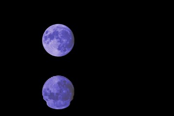 big blue full moon in starless sky at night and the reflection on the water