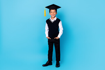 Poster - Full size photo of cheerful positive boy put hands pockets wear mortarboard isolated on blue color background