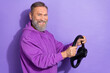 © deagreez - Portrait of old handsome good mood man wear purple sweater holding steering wheel buy new vehicle isolated on violet color background