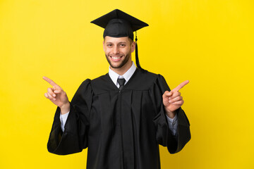 Wall Mural - Young university graduate caucasian man isolated on yellow background pointing finger to the laterals and happy