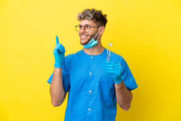 Canvas Print - Dentist caucasian man holding tools isolated on yellow background pointing up a great idea