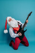© ZaStock - Full size of emotional Santa Claus who plays on electric guitar on blue background. Christmas party.