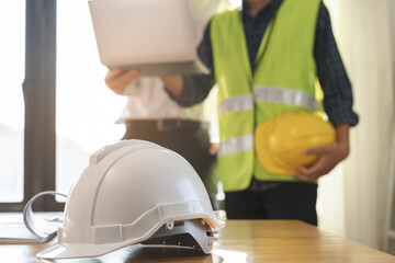 Close up white safety hard helmet. Asian, caucasian young engineer, architect two man are discussing construction to follow the project to build an industrial plan at site. Engineer worker people.