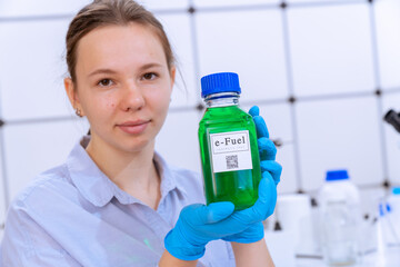 Canvas Print - young woman holding a chemical bottle with a green liquid in her hands text on the label e-fuel Biofuel chemical laboratory