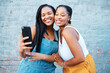 © N Lawrenson/peopleimages.com - Black women, friends and selfie while smiling and happy outside against city or urban wall and posing for friendship social media picture outside. African females or sisters with 5g network connectio