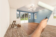 Before and After of Man Painting Roller to Reveal Newly Remodeled Room with Fresh Blue Paint and New Floors.