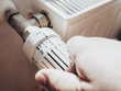 Main d'homme baissant le thermostat de son chauffage radiateur - Personne qui règle la température de son logement pour faire des économies, à cause de l'augmentation des prix de l'énergie et du gaz