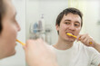 © Асель Иржанова - young man brushes his teeth in front of a mirror in the bathroom. oral hygiene, dental care