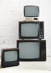 Four old TVs stand against a background of white brick.