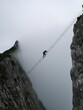 Vertical shot of a climber crossing from one cliff to another over a rope bridge in a foggy weather