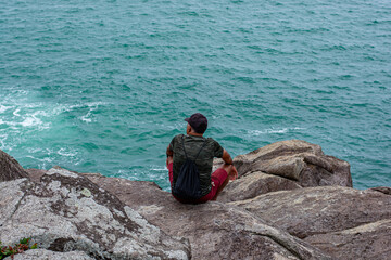 Wall Mural - man sitting on the rocks looking at the sea in Florianópolis